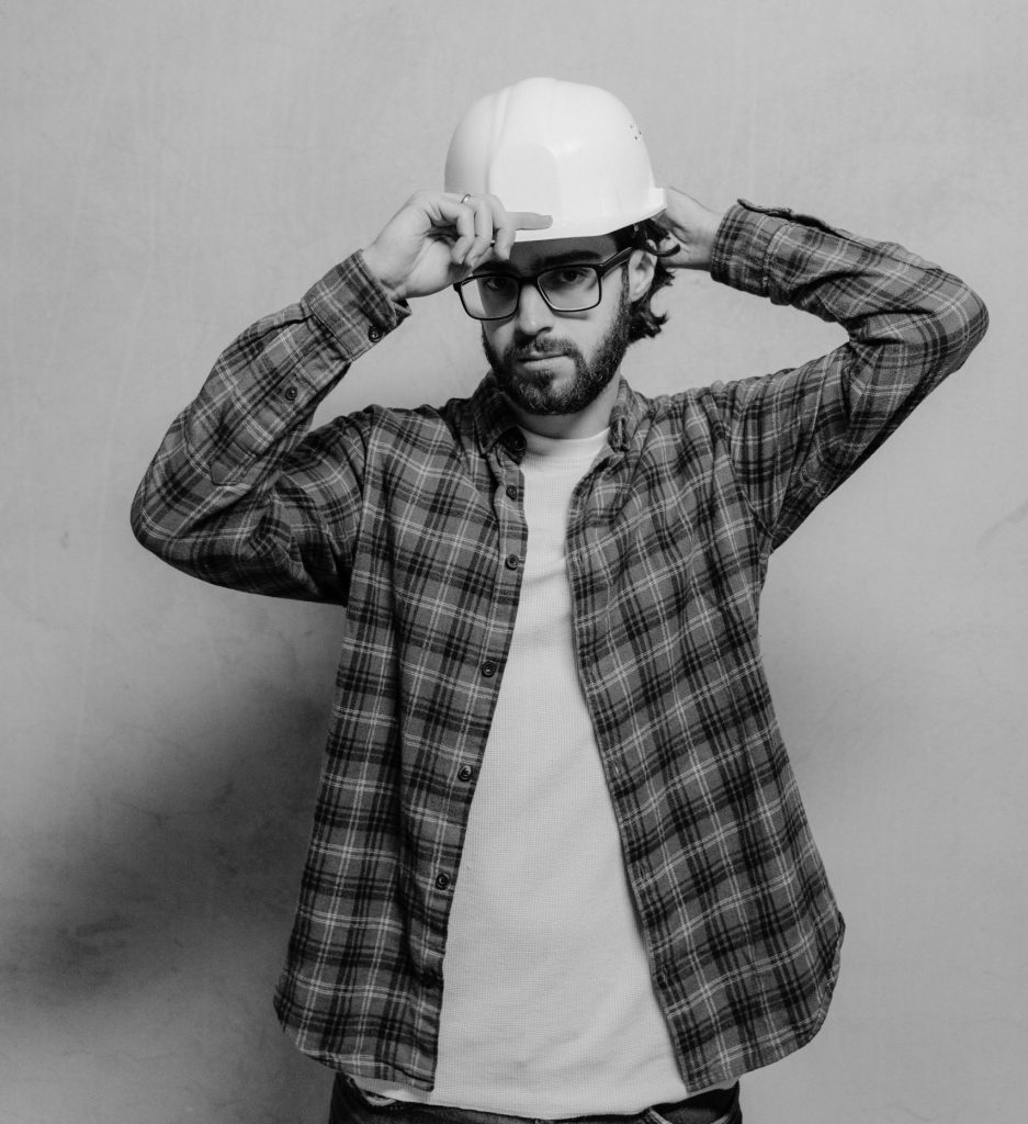 Black and white photo of a male construction worker wearing a hard hat and glasses.